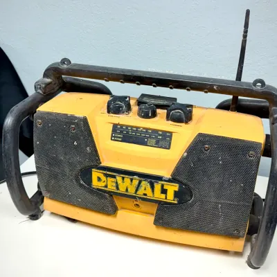 Sale Photo Thumbnail #907: Vintage DeWalt heavy-duty jobsite AM/FM radio featuring a rugged roll-cage frame, top control knobs, and front-facing dual speakers showing light cosmetic wear.