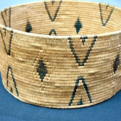 Sale Photo Thumbnail #381: Handwoven cylindrical basket featuring dark geometric chevron and diamond patterns against a natural fiber weave.