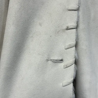 Sale Photo Thumbnail #852: Close-up detail of an off-white faux suede or shearling coat featuring whipstitch trim and a buttonhole, showing light surface wear and smudges.