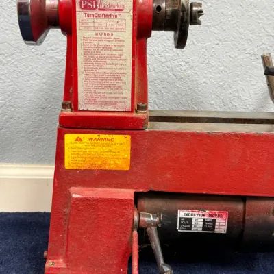 Sale Photo Thumbnail #552: PSI Woodworking Products TurnCrafter Pro mini lathe in red, showing the headstock, motor, and safety warning labels.