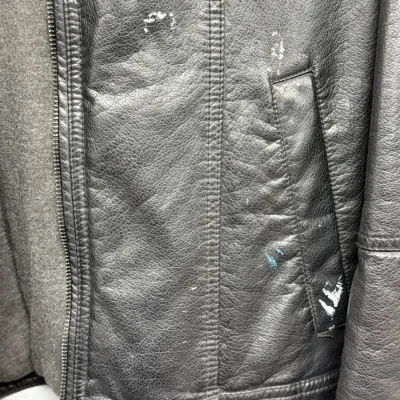 Sale Photo Thumbnail #880: Close-up of a black faux-leather or leather jacket showing surface wear, small scuffs, and white paint splatter near the side pocket.