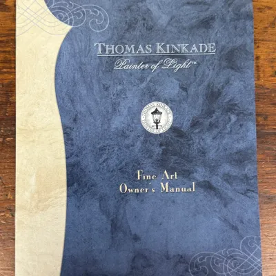 Sale Photo Thumbnail #820: Thomas Kinkade Fine Art Owner's Manual booklet with blue mottled cover and ornamental scroll details.