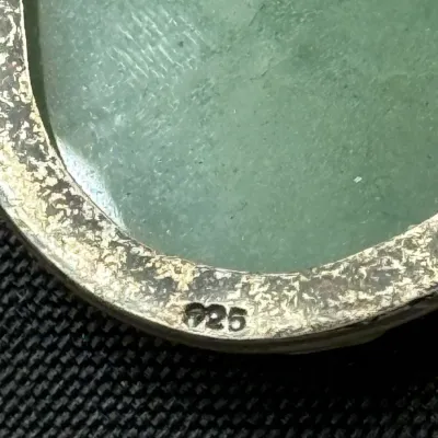 Sale Photo Thumbnail #331: Close-up of a green jade or gemstone piece set in a sterling silver bezel, marked with a 925 hallmark.