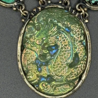 Sale Photo Thumbnail #326: Vintage iridescent green molded glass dragon pendant necklace set in silver-tone metal alongside turquoise cabochons.