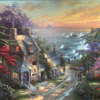 Sale Photo Thumbnail #824: Framed Thomas Kinkade print depicting a coastal village with a lighthouse and cottages, set in a gold-tone frame.