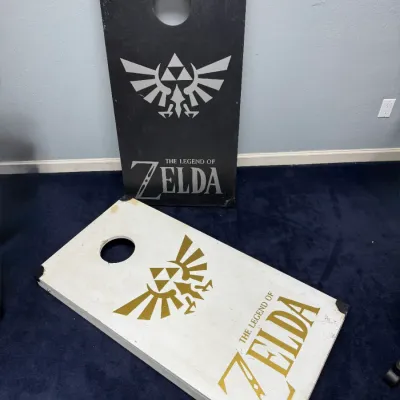 Sale Photo Thumbnail #927: Pair of custom-painted 'The Legend of Zelda' cornhole boards featuring the Hyrule crest, showing minor surface scuffs.