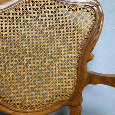 Sale Photo Thumbnail #675: Vintage French provincial style armchair featuring a carved wooden frame with a woven cane backrest and seat.