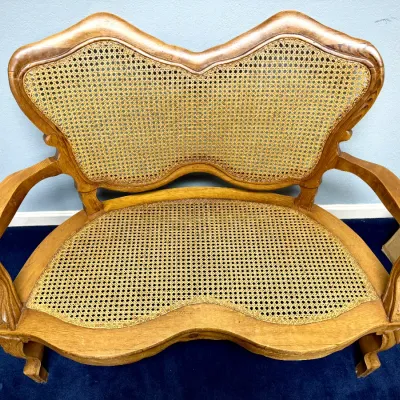 Sale Photo Thumbnail #672: Vintage French Provincial style wooden loveseat featuring a curved frame and woven cane seat and backrest.