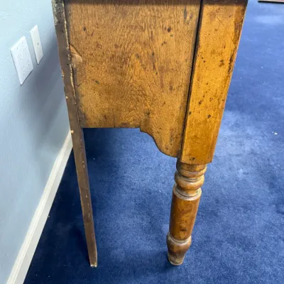 Sale Photo Thumbnail #287: Side profile of an antique wooden desk featuring turned front legs and a dark-stained top, showing wear and distressing on the finish consistent with age.