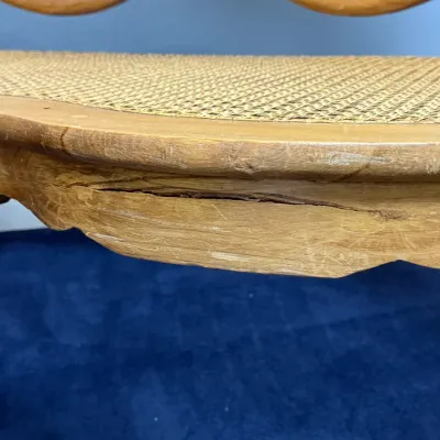 Sale Photo Thumbnail #677: Close-up of a vintage light wood bench featuring a woven cane seat, cabriole legs, and visible cracking and wear along the front apron.