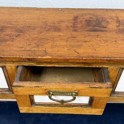 Sale Photo Thumbnail #279: Antique wooden cabinet or desk featuring a center drawer with white paneling and decorative brass bail pull, showing a distressed rustic finish.