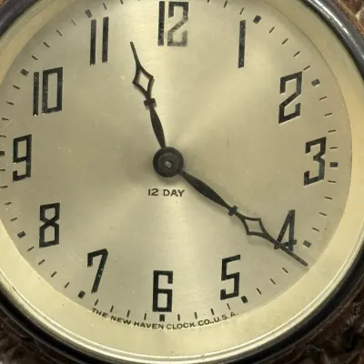 Sale Photo Thumbnail #393: Vintage New Haven Clock Co. 12-day clock face featuring bold Art Deco style numerals and ornate hands set in a textured leather or faux-leather frame.