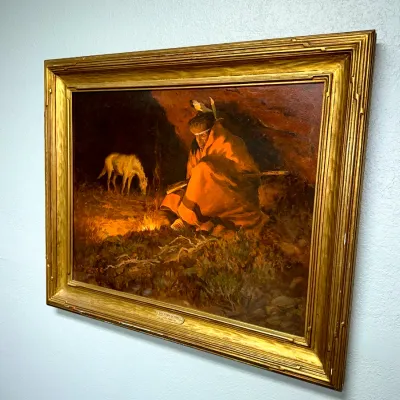 Sale Photo Thumbnail #100: Framed oil painting print depicting a Native American seated by a campfire wrapped in an orange blanket, housed in a ornate gilded wooden frame.