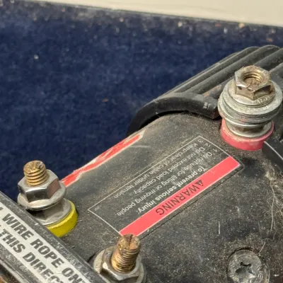 Sale Photo Thumbnail #668: Close-up of a heavy-duty electric winch motor housing showing electrical terminal posts, warning labels, and wire rope directional markings.