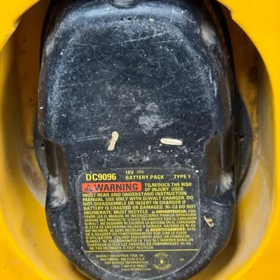 Sale Photo Thumbnail #913: DeWalt DC9096 18V Type 1 rechargeable battery pack inserted into a yellow tool housing, showing wear and scuffs from use.