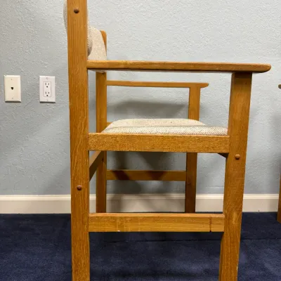 Sale Photo Thumbnail #699: Side profile of a solid oak armchair featuring a light beige upholstered seat and back cushion, with subtle wear on the wooden frame.