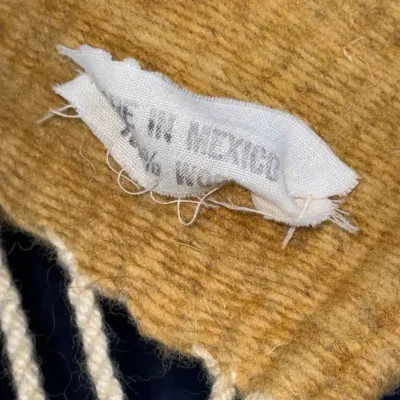 Sale Photo Thumbnail #425: Detail view of a woven wool textile showing a 'Made in Mexico' fabric label and fringed border.