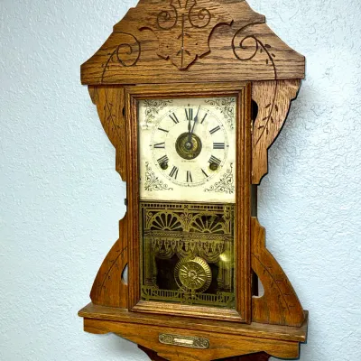 Sale Photo Thumbnail #366: Antique Seth Thomas gingerbread wall clock in an oak case with carved accents and decorative glass pendulum door, late 19th to early 20th century.