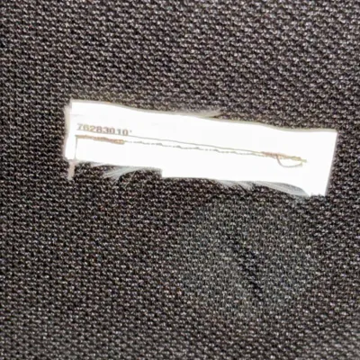 Sale Photo Thumbnail #236: Close-up of a white fabric tag with serial number 76283010 sewn onto dark textured upholstery.