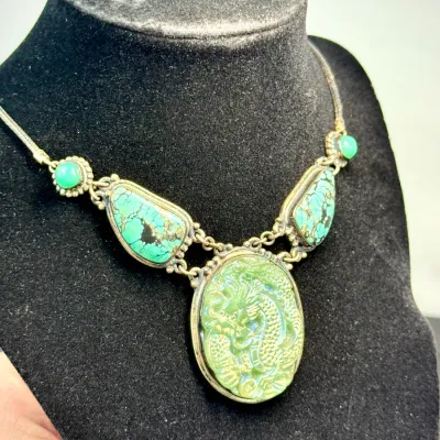 Sale Photo Thumbnail #332: Vintage Asian-inspired statement necklace featuring a carved green jade dragon central pendant flanked by turquoise and green cabochons set in silver-tone metal.