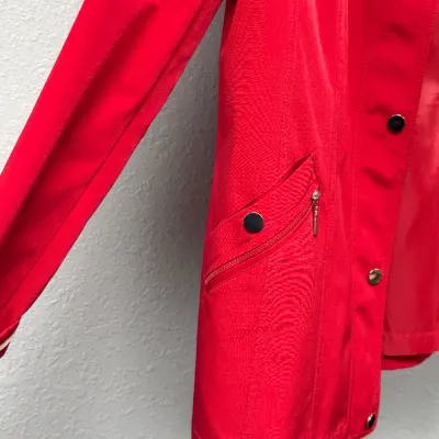 Sale Photo Thumbnail #894: Close-up detail of a women's bright red coat featuring front snap closures and a zippered side pocket with a decorative snap flap.