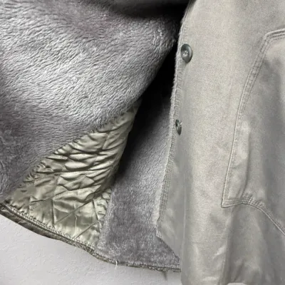 Sale Photo Thumbnail #871: Close-up view of a heavy winter coat featuring a grey canvas exterior, front button closure, and a plush fleece lining combined with quilted interior details.