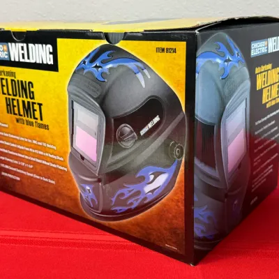 Sale Photo Thumbnail #523: Chicago Electric Welding auto-darkening welding helmet featuring blue flame graphics, presented in its original retail box.