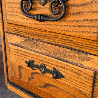 Sale Photo Thumbnail #261: Solid oak furniture drawers featuring decorative dark wrought iron hardware and prominent wood grain detail.