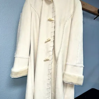 Sale Photo Thumbnail #845: Off-white faux suede hooded coat with fleece trim and toggle closures, hanging on a clothing rack.