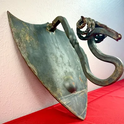 Sale Photo Thumbnail #415: Vintage wrought iron wall sconce featuring a shield-shaped backplate and a dragon or serpent head candle holder arm. Shows signs of surface rust and patina consistent with age.