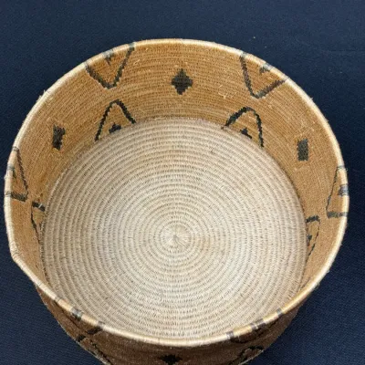 Sale Photo Thumbnail #386: Handwoven cylindrical basket featuring dark geometric chevron and diamond patterns along the sides with a tightly coiled interior.