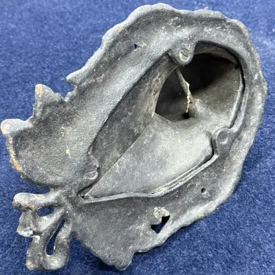 Sale Photo Thumbnail #653: Underside of a vintage cast iron decorative piece featuring a bow-motif flourish and hollow cavity.