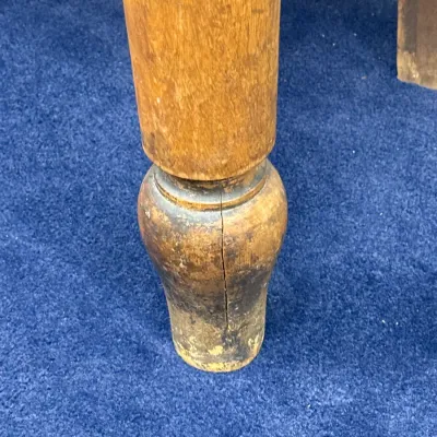 Sale Photo Thumbnail #289: Close-up of a turned wooden furniture leg, showing wear, distressing, and a vertical crack in the wood near the foot.