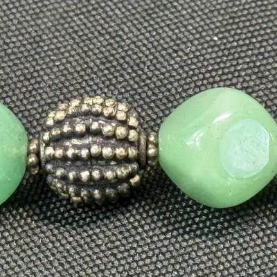 Sale Photo Thumbnail #335: Close-up of a beaded necklace featuring light green stone beads and an intricate textured metal spacer bead.