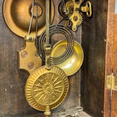 Sale Photo Thumbnail #370: Internal mechanism of an antique Seth Thomas mantle clock, featuring a embossed brass pendulum bob, chime bells, brass movement gears, and a winding key.