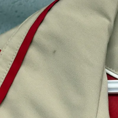 Sale Photo Thumbnail #898: Close-up detail of a beige jacket with red trim, showing a small faint spot on the fabric.
