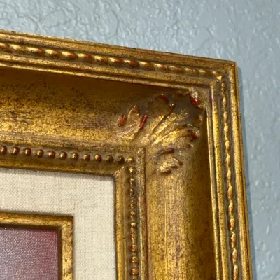 Sale Photo Thumbnail #141: Close-up detail of an ornate gilt wood picture frame featuring beaded trim, scrollwork corner accents, and a linen liner.