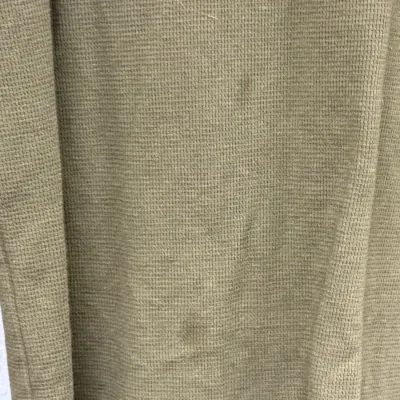 Sale Photo Thumbnail #888: Close-up of an olive green waffle-weave thermal shirt, showing light wear and small faint stains on the fabric.