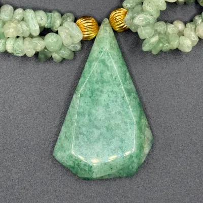 Sale Photo Thumbnail #344: Statement necklace featuring a large, faceted green aventurine teardrop pendant anchored by gold-tone ribbed accent beads and multi-strand green stone chip strands.
