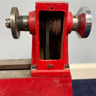Sale Photo Thumbnail #561: Vintage red cast-iron mini lathe headstock featuring a step pulley, drive belt mechanism, and handwheel.