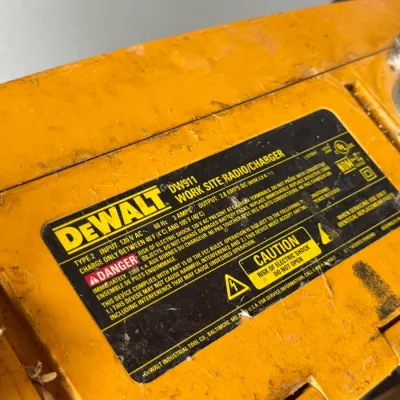 Sale Photo Thumbnail #914: DeWalt DW911 work site radio and battery charger, showing heavy cosmetic wear and dirt from job site use.