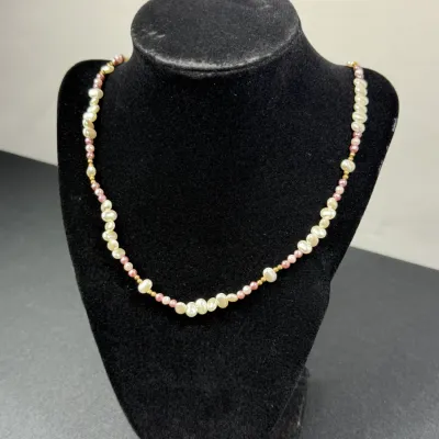 Sale Photo Thumbnail #196: Freshwater pearl necklace featuring irregular white pearls interspersed with small pink seed beads and gold-tone spacer beads, displayed on a black velvet bust.
