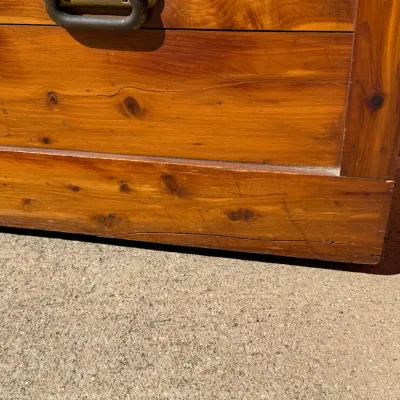 Sale Photo Thumbnail #324: Close-up of a rustic wooden trunk featuring warm knotty pine or cedar grain, showing some surface wear and a metal handle.