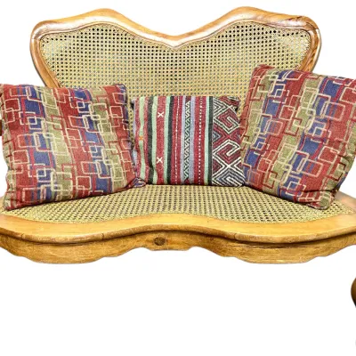 Sale Photo Thumbnail #61: French Provincial style carved wooden loveseat featuring a cane back and seat, accompanied by three patterned throw pillows.