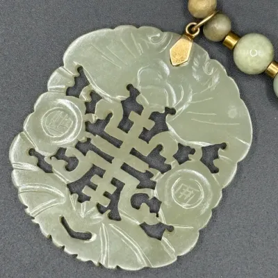 Sale Photo Thumbnail #358: Hand-carved light green celadon jade pendant featuring an intricate openwork pierced motif, suspended from a matching beaded necklace.