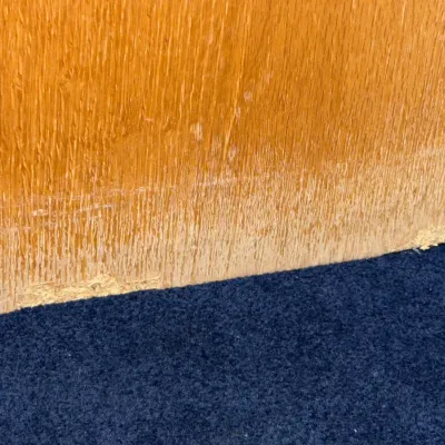 Sale Photo Thumbnail #721: Close-up detailing condition damage and wear along the bottom edge of a wood laminate furniture piece.