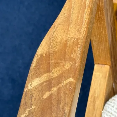 Sale Photo Thumbnail #703: Close-up detail of a wooden chair arm, showing noticeable finish wear and scratches on the warm wood grain.