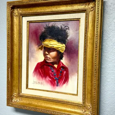 Sale Photo Thumbnail #148: Framed oil painting portrait of a Native American child wearing a yellow headband, signed by artist Goebel, set in an ornate gilded frame with linen matting.