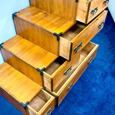 Sale Photo Thumbnail #210: Japanese-style step chest (kaidan tansu) featuring honey-toned wood construction, box-joint detailing, dark metal hardware, and multiple pull-out storage drawers.