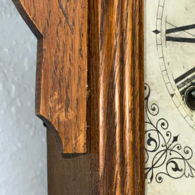 Sale Photo Thumbnail #373: Close-up detail of an antique oak wall clock showing carved wooden trim and a printed face with Roman numerals.